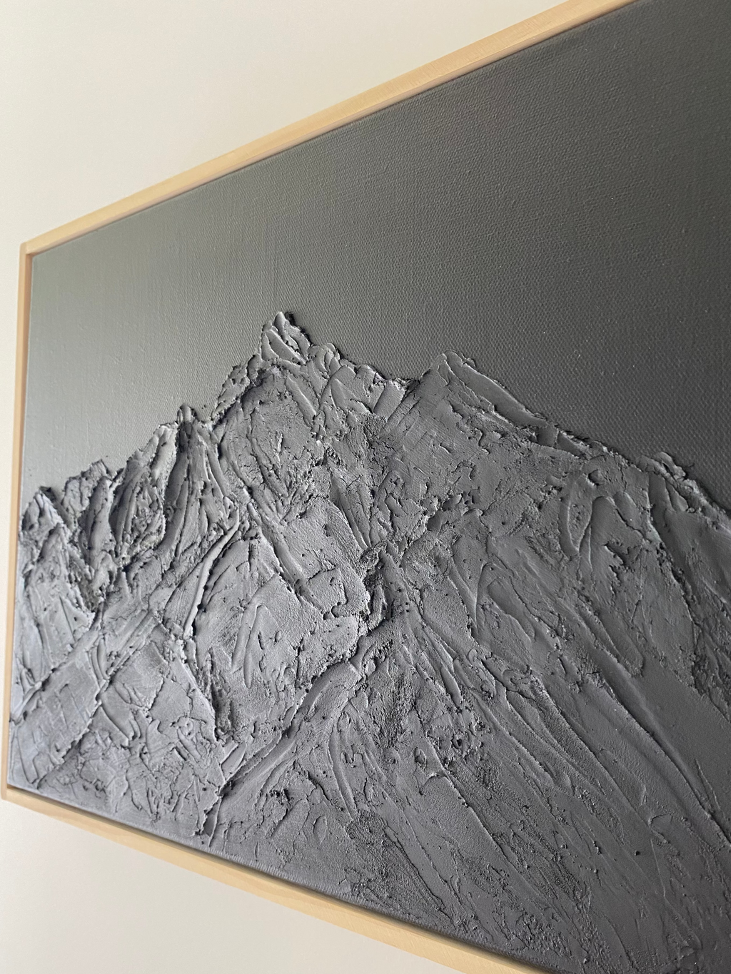 Textured wall art with a mountain landscape in a wooden frame on a white wall.