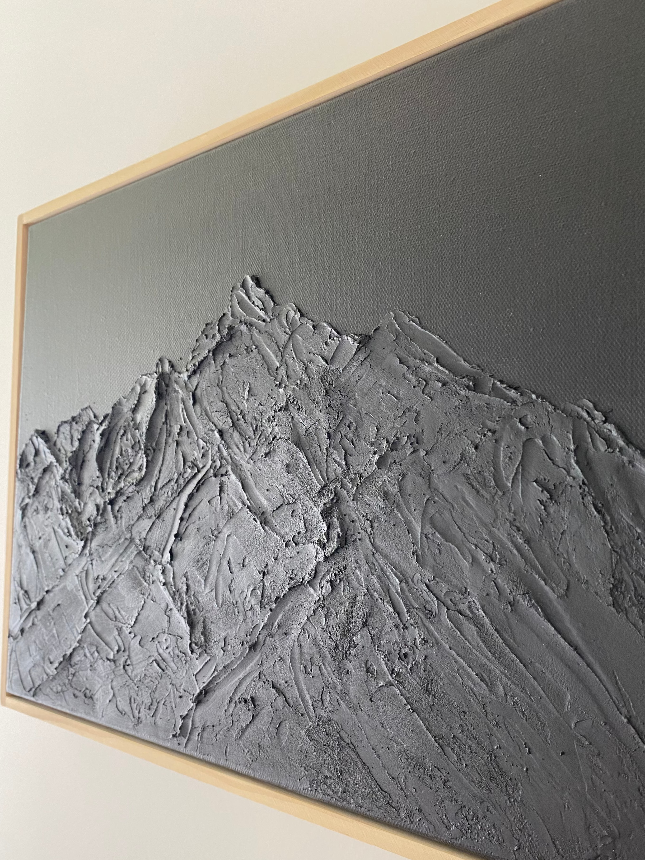 Textured wall art with a mountain landscape in a wooden frame on a white wall.